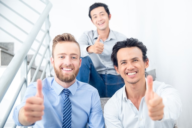 Free photo smiling colleagues showing thumbs up on stairs