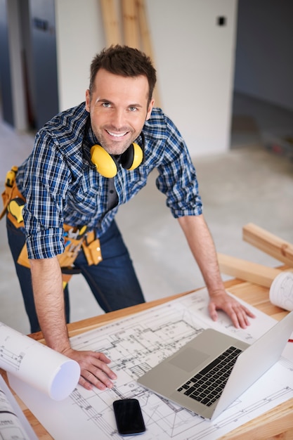 Smiling construction worker with plans and a laptop