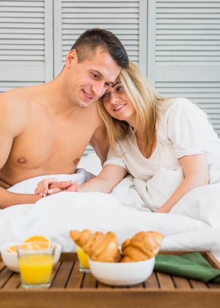 Smiling couple holding hands in bed near breakfast on board