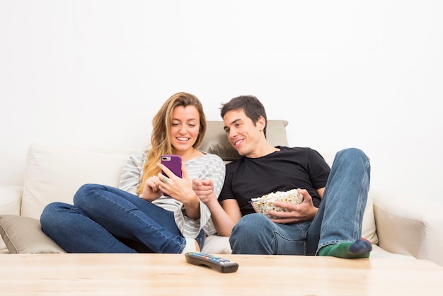 Smiling couple looking at mobile phone sitting on the sofa