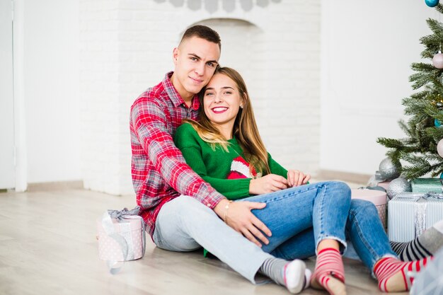 Smiling couple sitting next to christmas tree