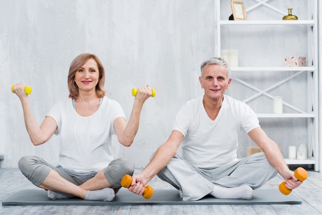 Free photo smiling couple sitting on yoga mat exercising with dumbbells