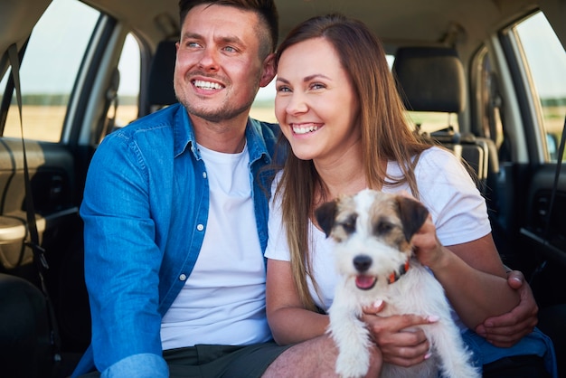 Smiling couple and their dog sitting in the car trunk