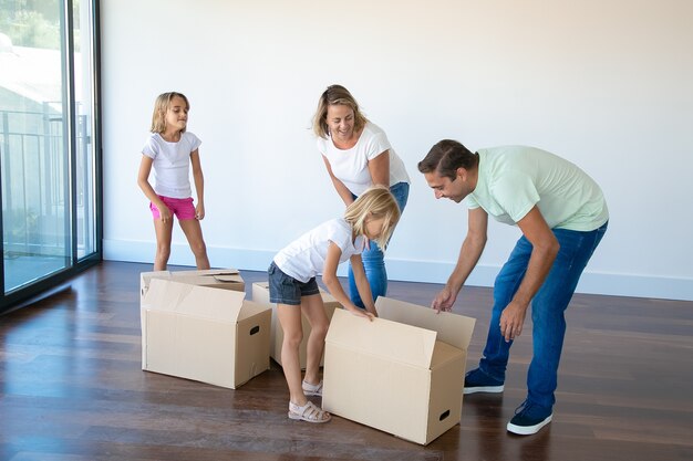 Smiling couple with two daughters unpacking boxes in empty room