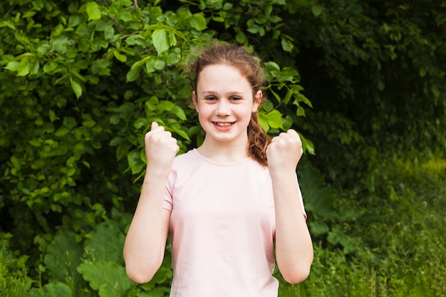 Free Photo smiling cute girl clenching her fist making yes gesture while standing in park