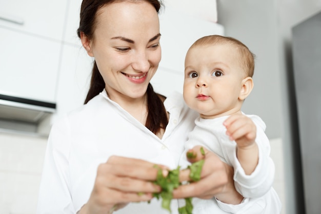 Smiling cute mother feeding baby with lettuce