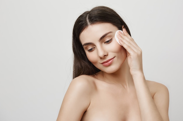 Smiling cute woman take-off makeup with cotton pad