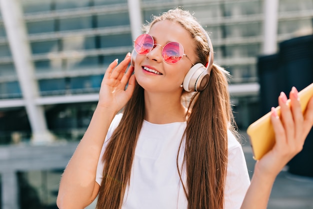 Smiling and dancing young woman holding a smartphone and listening music in headphones