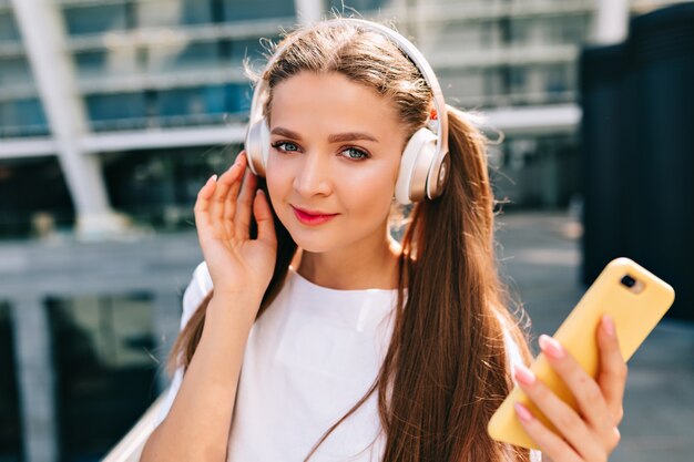 Smiling and dancing young woman holding a smartphone and listening music in headphones