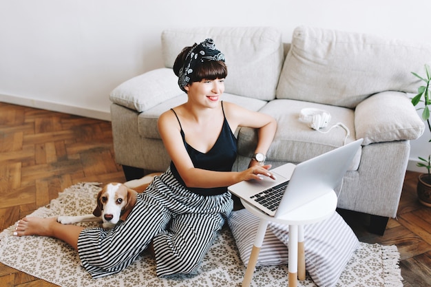 Free photo smiling dark-haired lady in trendy striped pants working with computer while her beagle dog lying beside