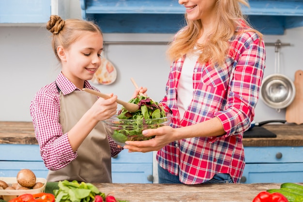 Smiling daughter and mother preparing the leafy vegetable salad in the kitchen