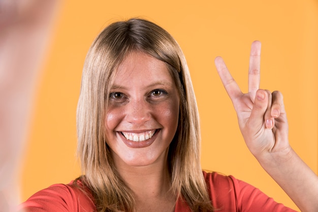 Free Photo smiling deaf woman showing victory sign over bright yellow backdrop