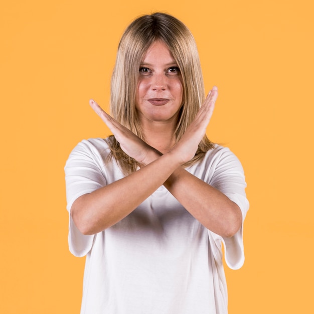 Free photo smiling disable woman showing warning gesture in sign language against yellow backdrop