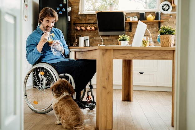 Smiling disabled freelance worker enjoying on lunch break with his dog while working at home