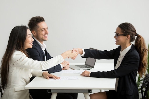 Smiling diverse businesswomen shake hands at group meeting, deal concept