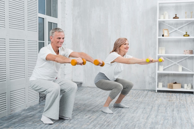 Free Photo smiling elder couple performing exercise with dumbbells at home