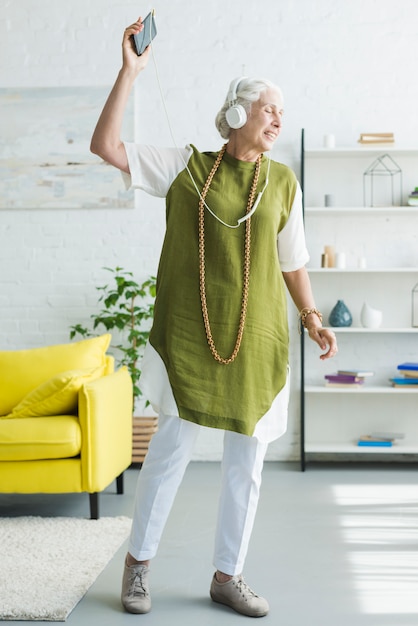 Free photo smiling elderly woman listening music on headphone dancing at home