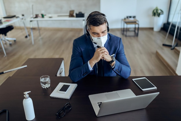 Free photo smiling entrepreneur with face mask using computer while having video call in the office