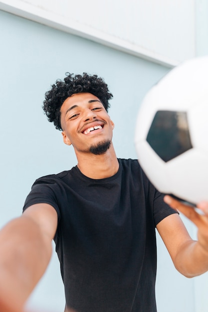 Free photo smiling ethnic man with football looking at camera