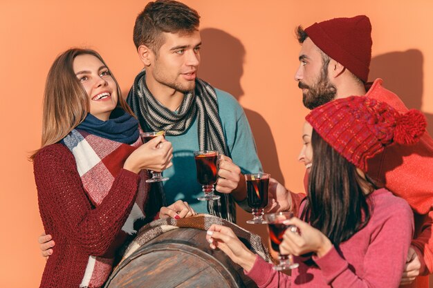 Free photo smiling european men and women during party photoshoot. guys posing as friends at studio fest with wineglasses with hot mulled wine on foreground.