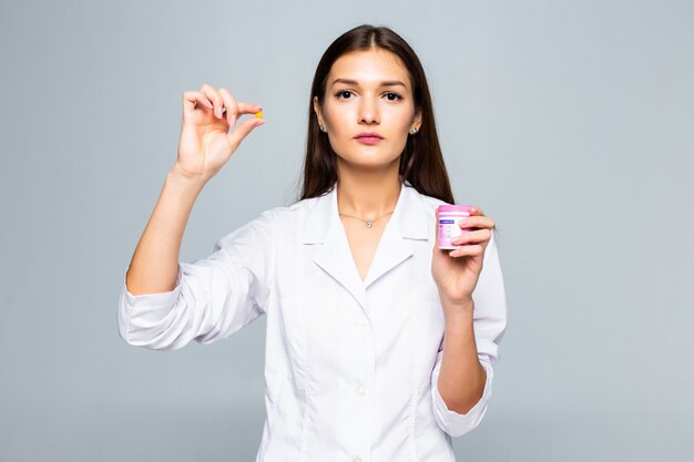 Smiling female doctor holding pills medication isolated on a white wall.