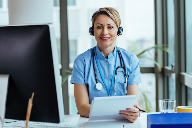 Smiling female doctor wearing headset while working at medical call center and looking at camera