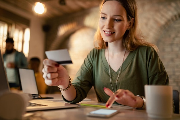 Free photo smiling female entrepreneur ebanking with credit card and mobile phone while working late in the office