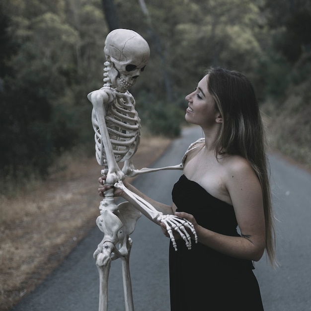 Free Photo smiling female holding artificial skeleton of man standing on road