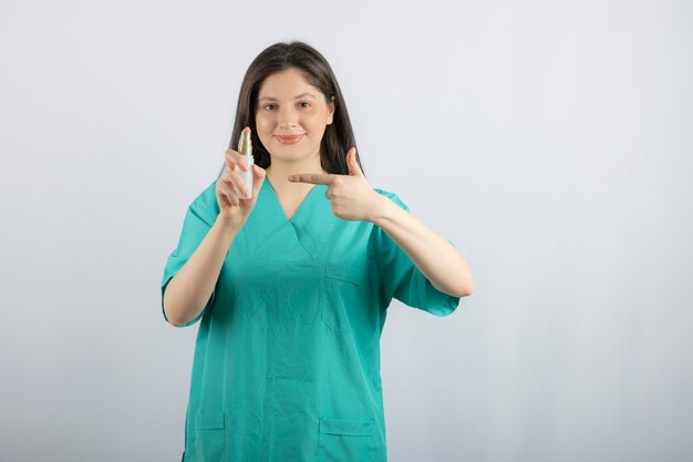 Smiling female nurse showing spray bottle on white. 