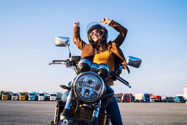 Free photo smiling female rider sitting on her motorcycle with arms high showing happiness