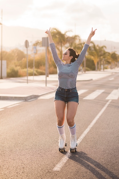 Smiling female skater wearing roller skate making peace gesture on road