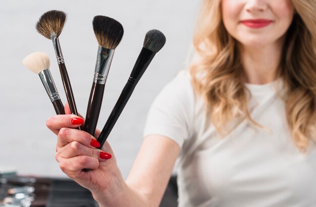 Smiling female visagiste holding cosmetic brushes