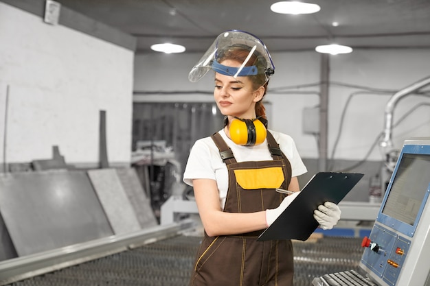 Smiling female worker of metal factory writing data