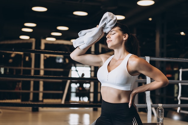 Smiling fit girl holding towel and taking rest in gym. Girl wipes sweat with a towel