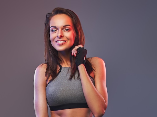 Smiling fitness brunette female in a gray sportswear posing in a studio. Isolated on a gray background.