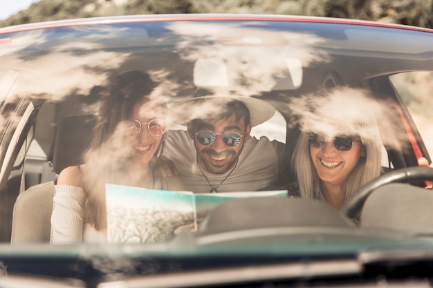 Free photo smiling friends looking at map sitting inside the car