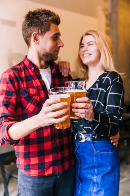 Smiling friends toasting the beer glasses looking at each other