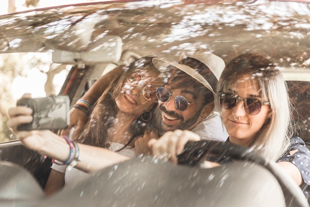 Smiling friends travelling in car taking selfie through mobile