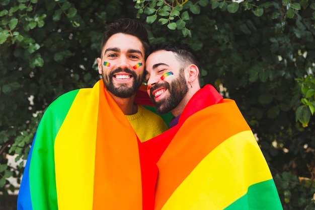 Smiling gay couple covering rainbow flag