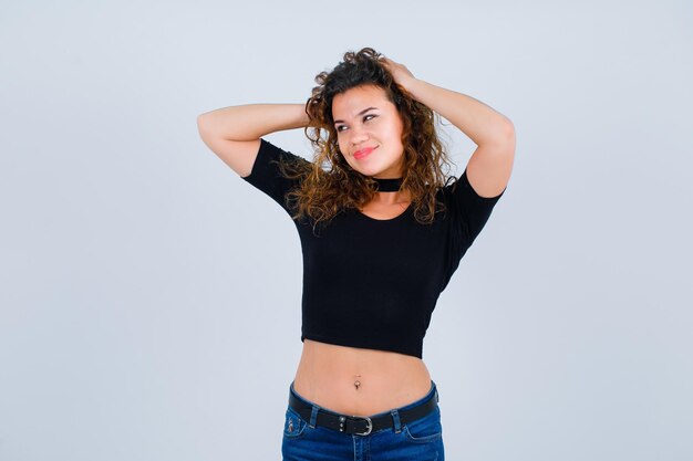 Smiling gilr is looking left by putting hands on head on white background