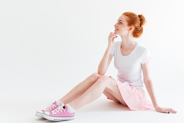 Smiling ginger girl sitting on the floor and looking away