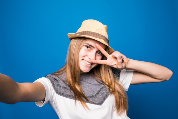 Smiling Girl in bright hat making selfie in front of blue wall