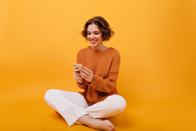 Free photo smiling girl in casual outfit sitting with legs crossed and holding phone