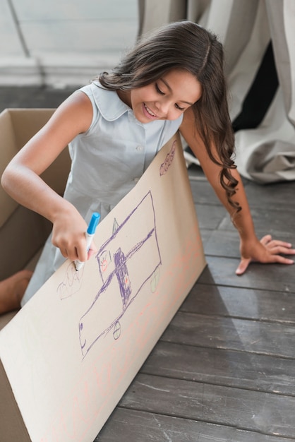 Free photo smiling girl drawing on cardboard with felt-tip pens marker