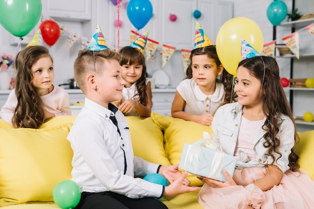 Smiling girl giving present to birthday boy in the party at home