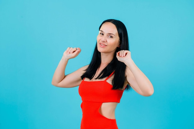 Smiling girl is dancing by raising up her fists on blue background