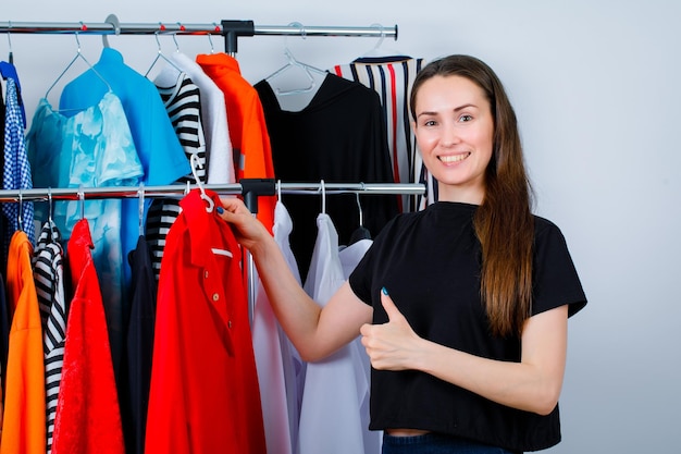 Smiling girl is holding blouse and showing perfect gesture on clothes background