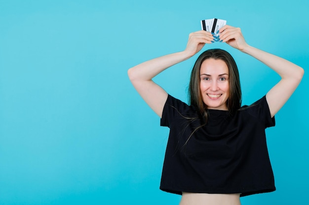 Smiling girl is holding credit cards over head on blue background