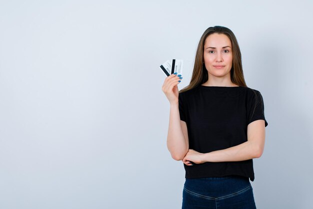 Smiling girl is looking at camera by holding credit cards on white background