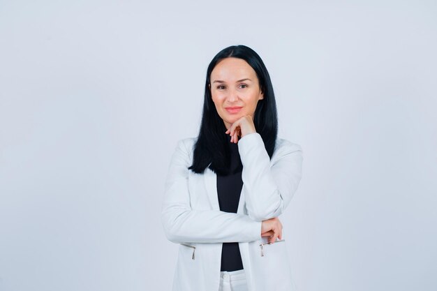 Smiling girl is looking at camera by holding hand on chin on white background